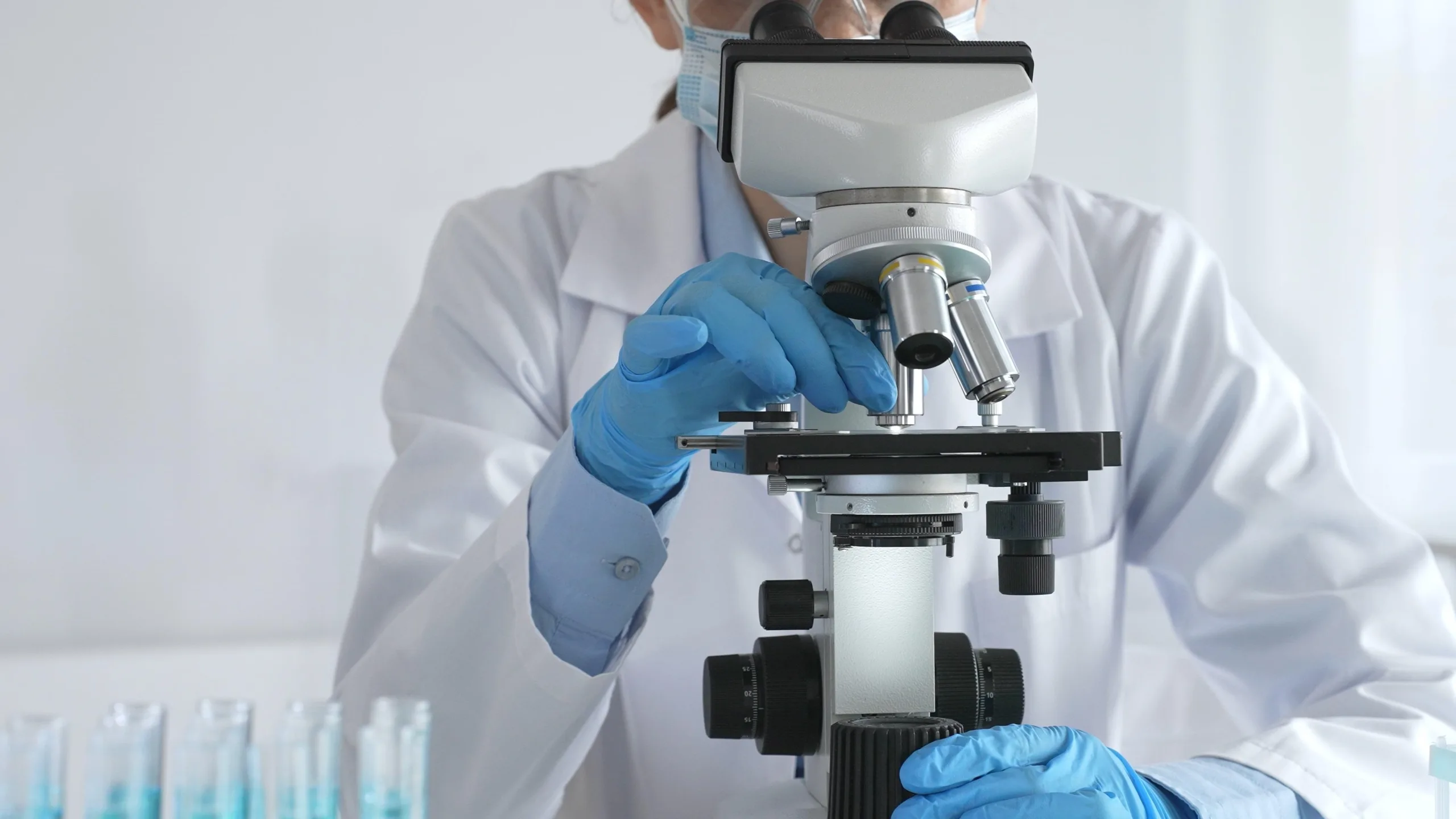 A,Female,Scientist,In,Protective,Gear,Adjusts,A,Microscope,Lens